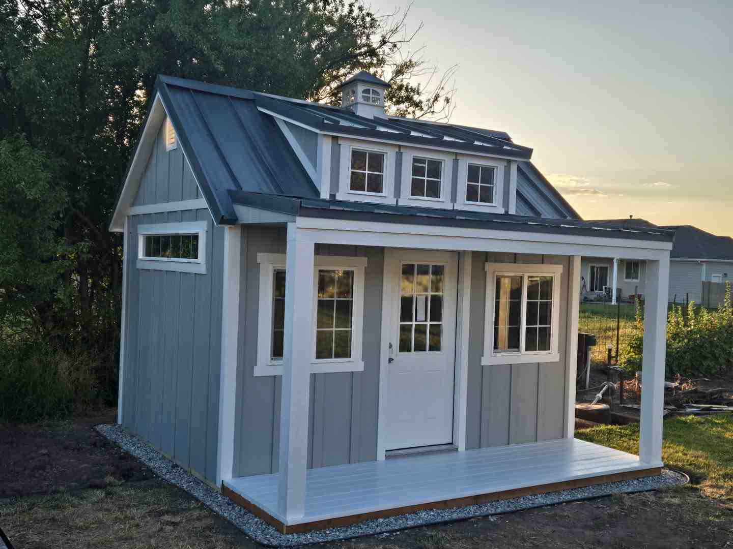 12x16 farm-style shed featuring a covered front porch, metal roof, and raised gravel foundation for added drainage
