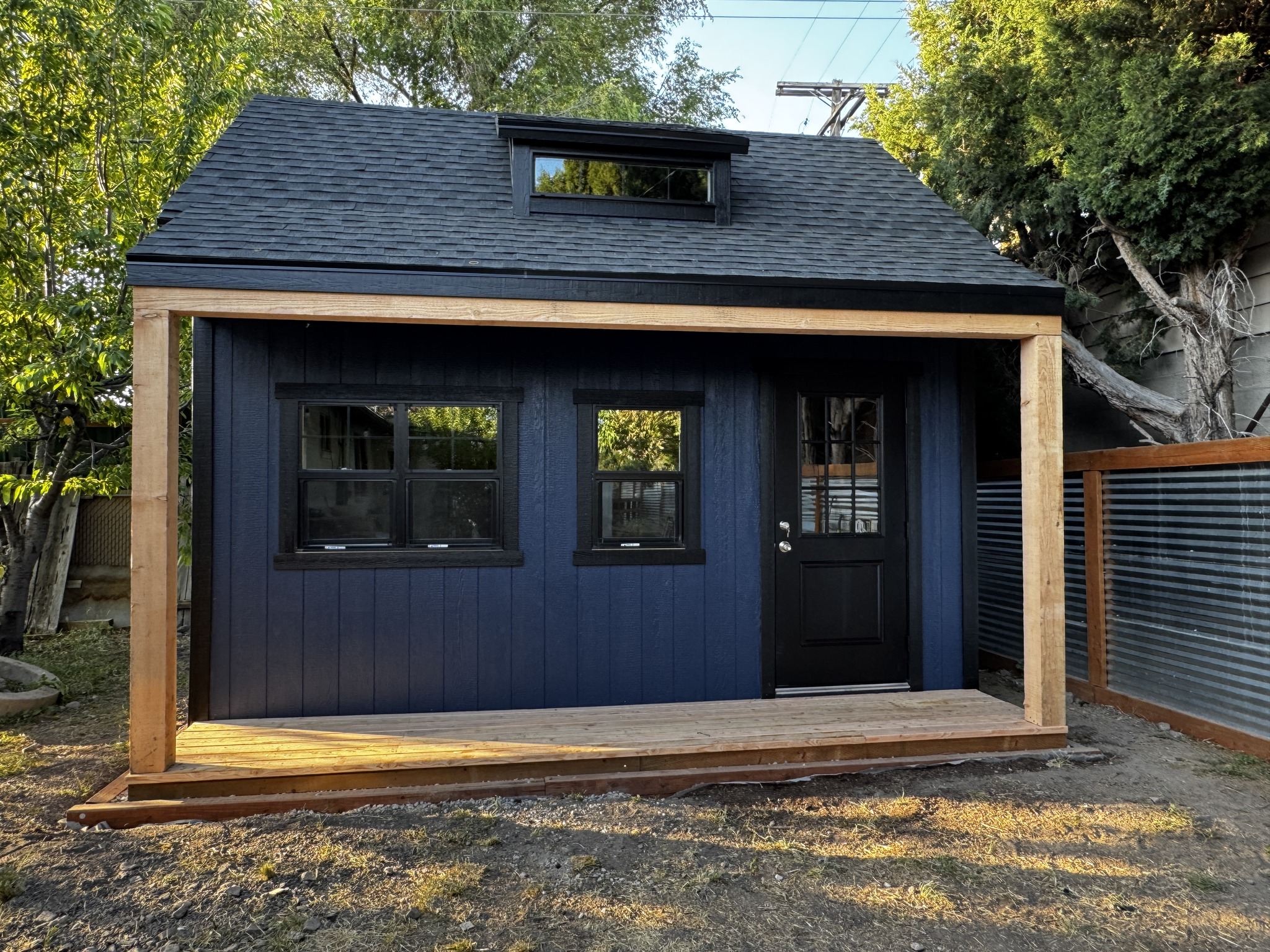 Deep navy custom storage shed with wood frame porch and black trim, showcasing durable and stylish custom storage solutions. 