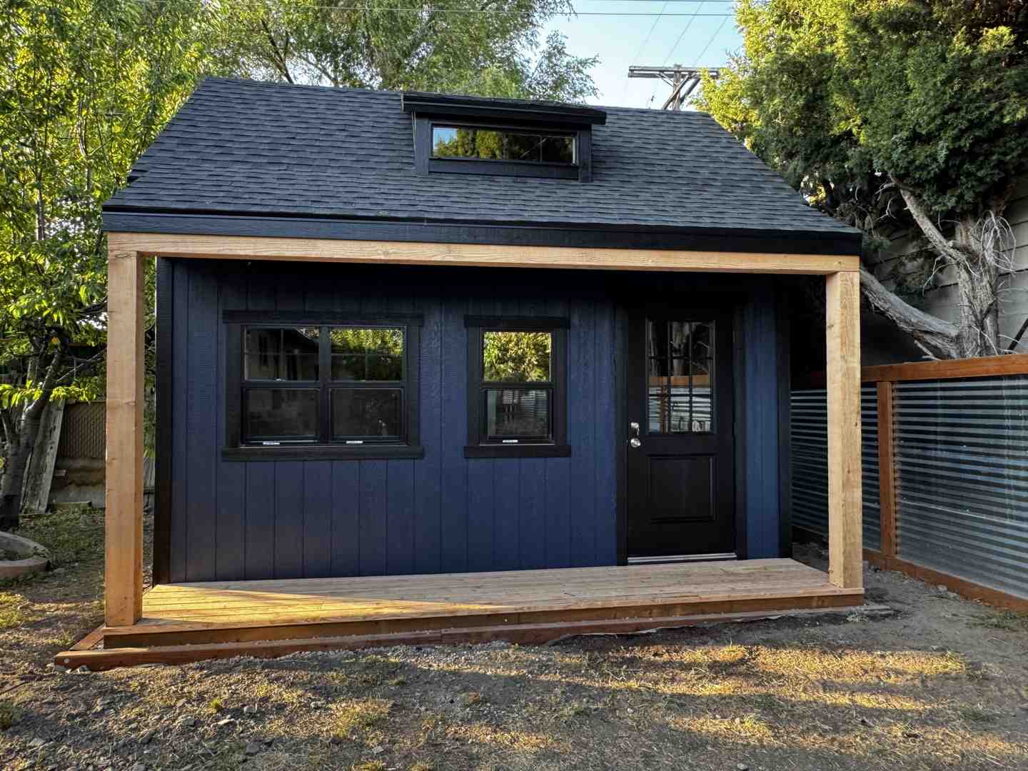 Deep navy backyard shed with porch and black door, custom windows, a storage shed built on site by Wright's Shed Co