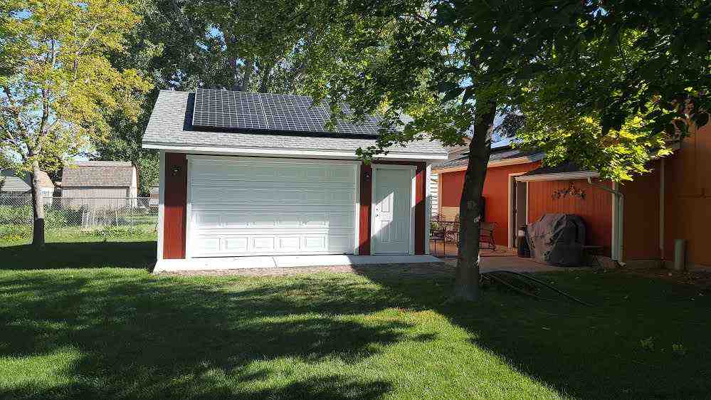 Detached garage with solar panels, red LP SmartSide siding, white garage door, and front entry access in backyard setting