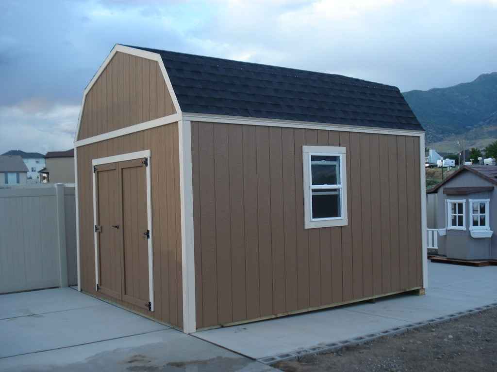 Sturdy brown farm shed with white trim, gambrel roof, double doors, and side window set against a mountain backdrop