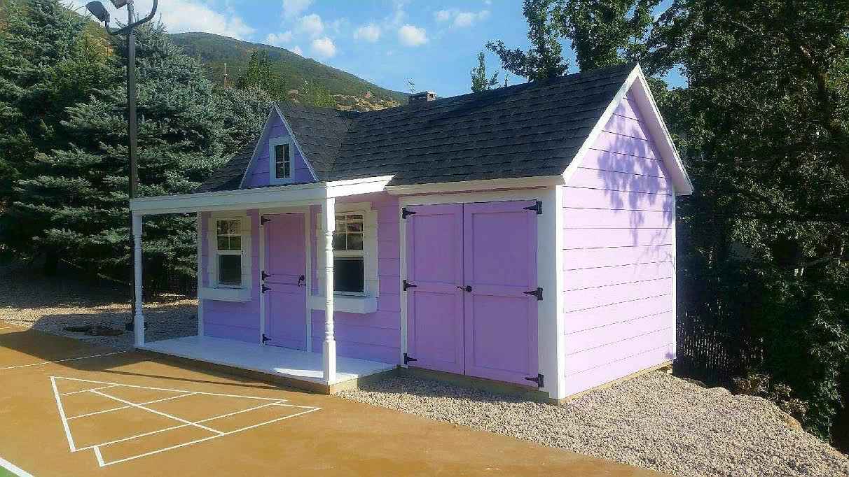 Lavender and white custom-built playhouse shed with porch and double doors, designed by Wright’s Shed Co. for outdoor family fun and storage.