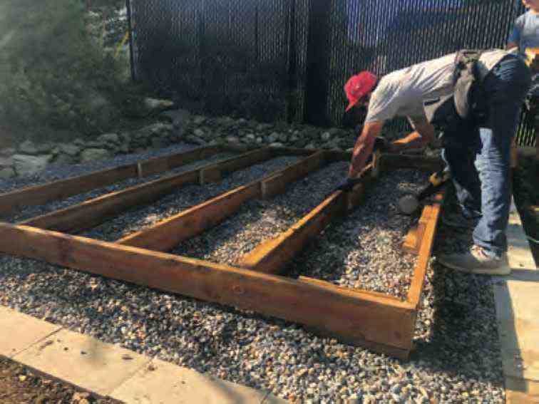 Worker installs treated lumber over a gravel pad while building a shed foundation using a DIY shed kit