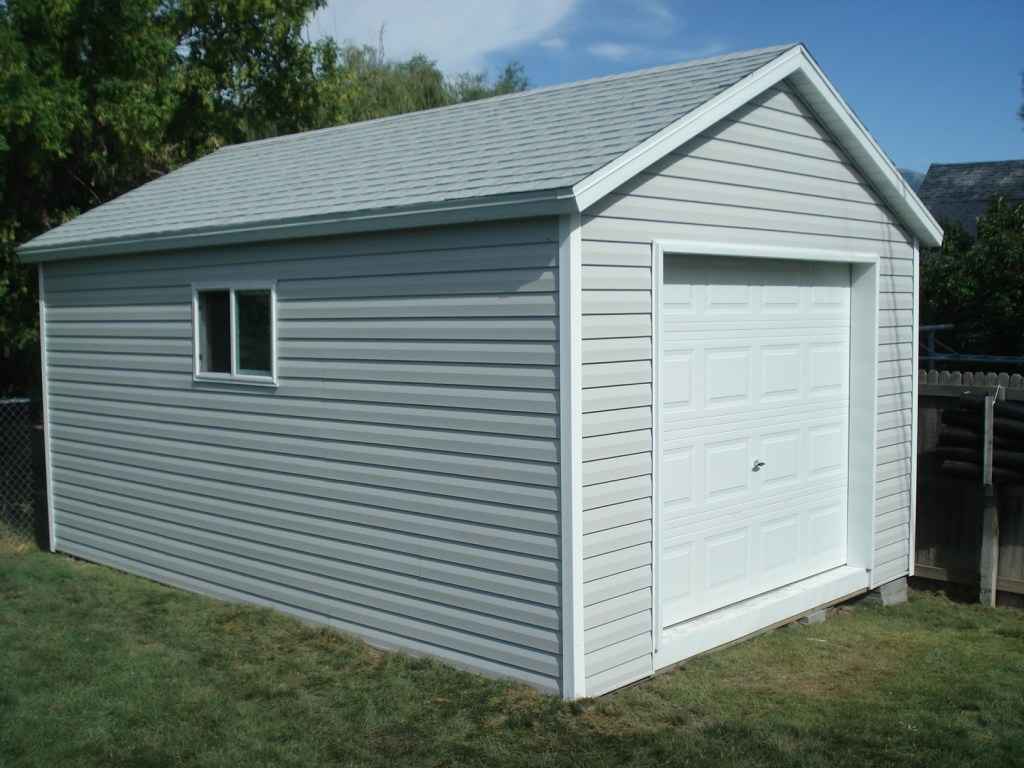 Detached gray one-car garage with vinyl siding and gable roof on lawn; example when building a garage for storage