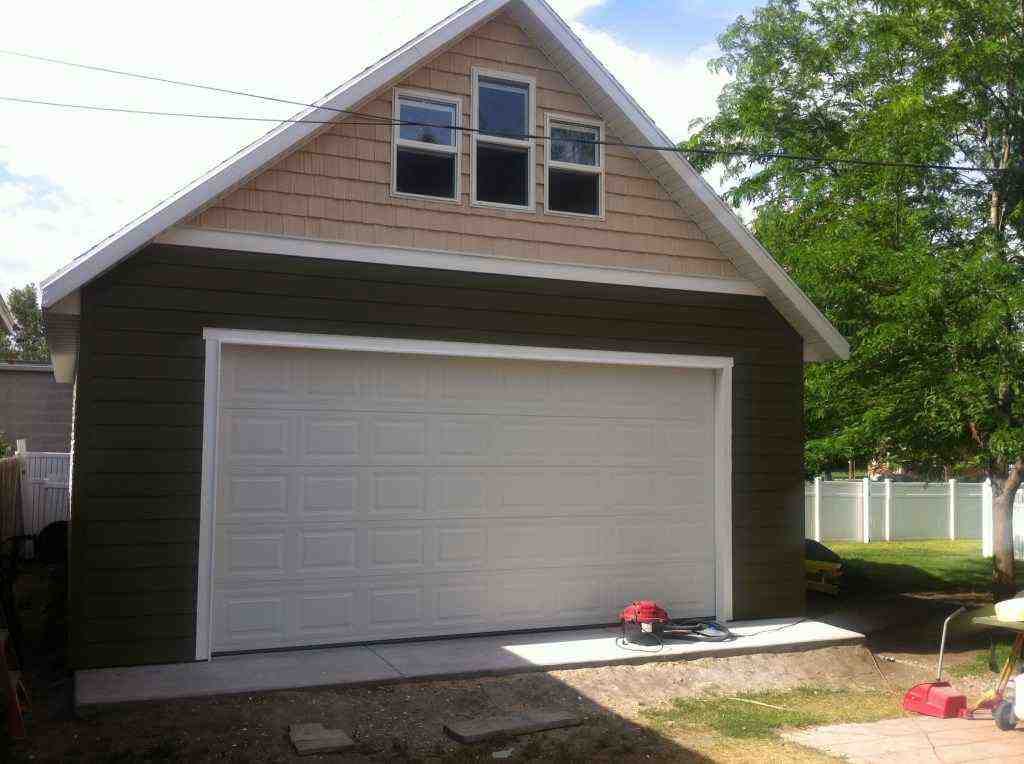 Green detached garage with loft and white overhead door, ideal for extra storage or workspace