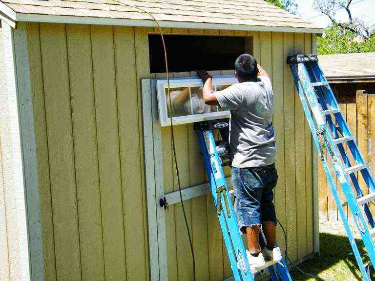 Worker attaching trim above the door on a pre-cut shed kit using a ladder