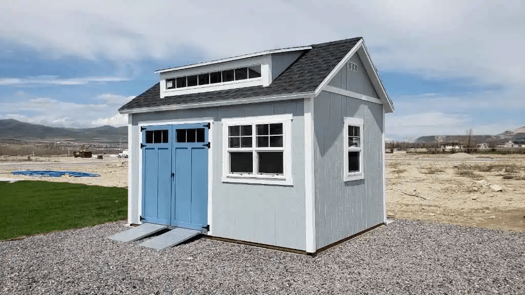 Light blue shed with dormer windows, ramp access, and black shingle roof- storage sheds logan utah