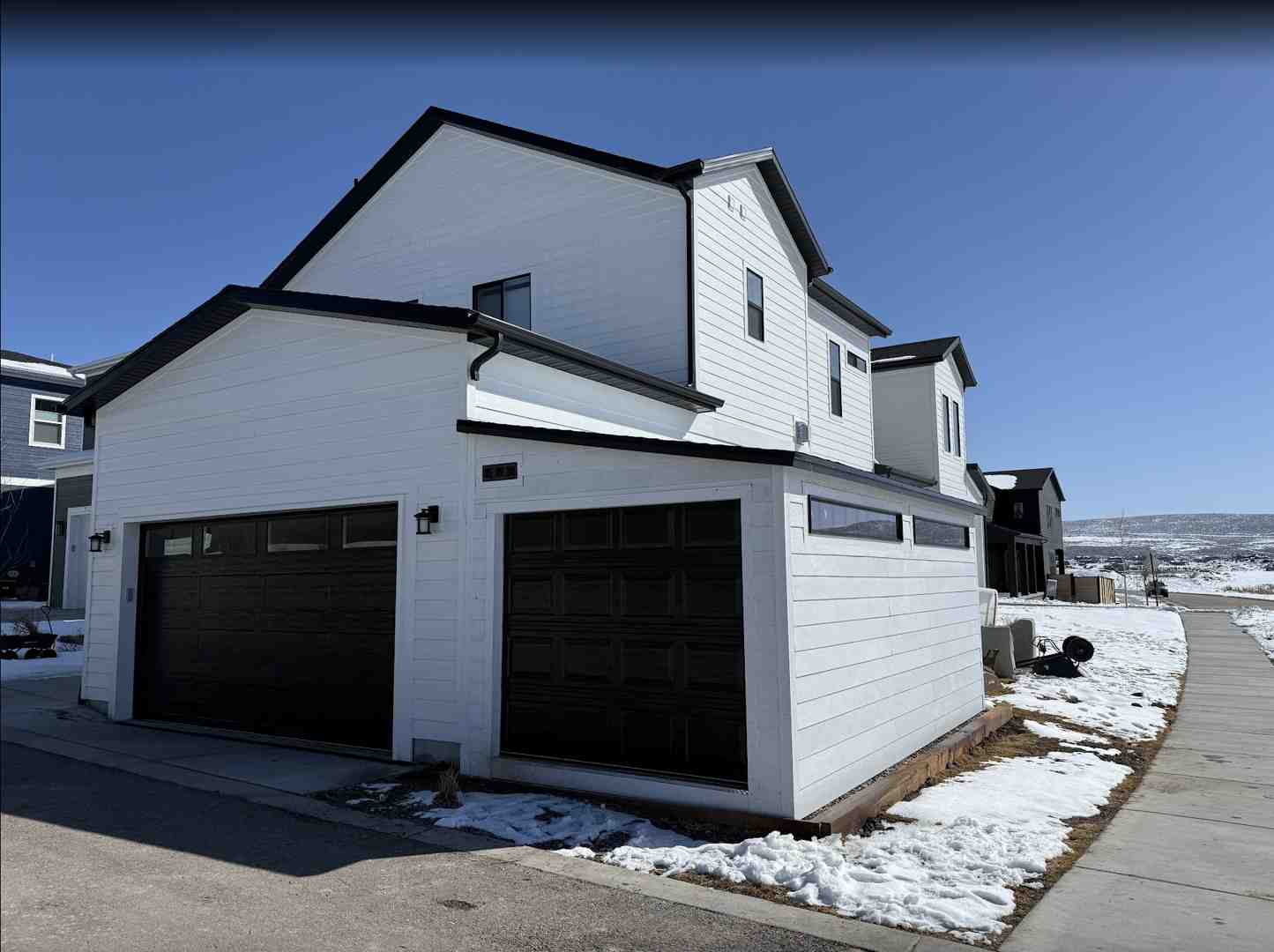 Custom built garage with black doors and attached white storage shed on a snowy residential street