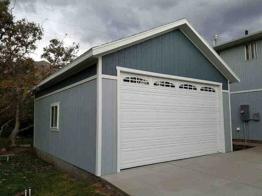 Blue detached garage with white trim, arched panel garage door, and concrete driveway featuring LP SmartSide siding.