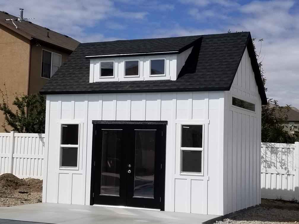 Modern white backyard shed with dormer windows and glass double doors on concrete; sleek option for sheds Idaho buyers