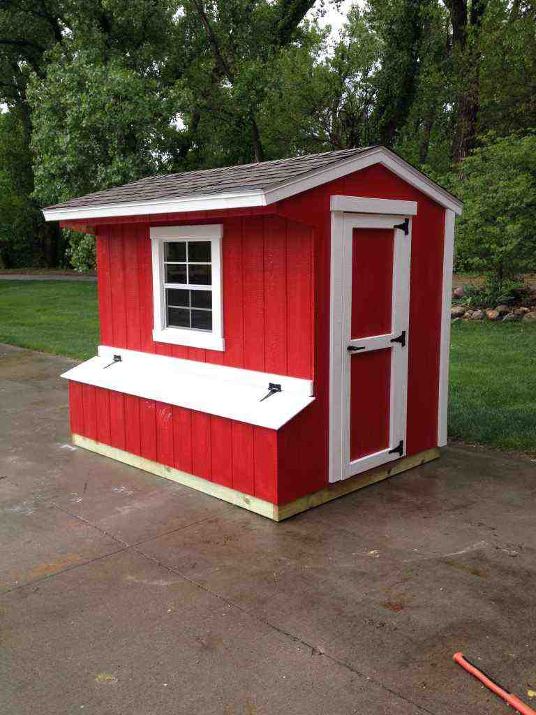 Bright red chicken coop enclosure with white trim, window, and lift-up nesting box access for backyard poultry housing.