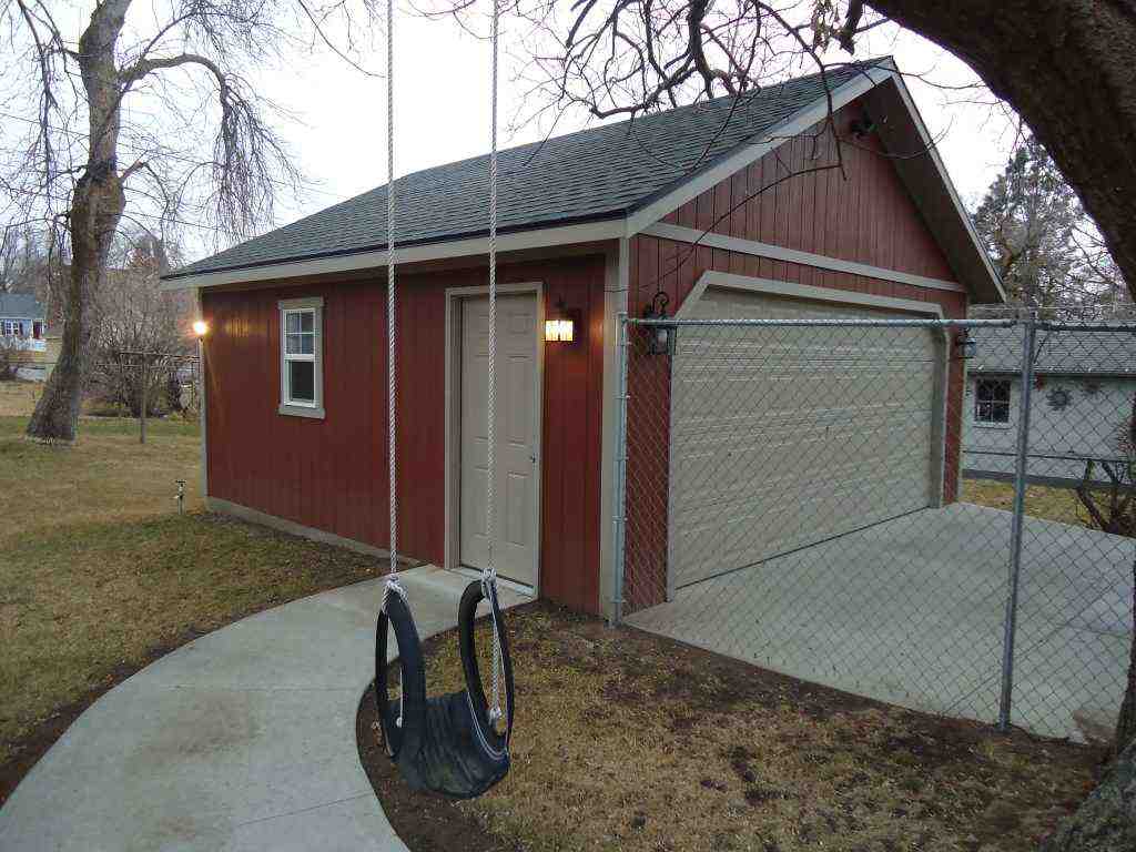 Red detached custom built garage with beige door and window, beside a swing and fenced concrete driveway