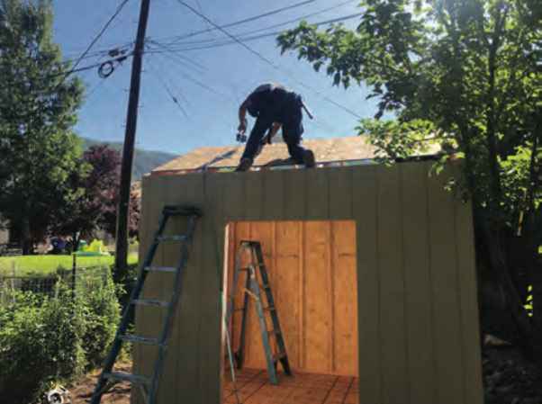 Worker securing roof panels on top of a partially built Wright’s Shed Co. DIY shed kit using ladders and tools for proper installation.