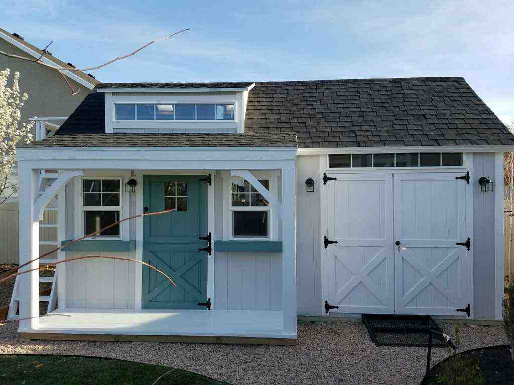 White and teal 10x20 structure—half playhouse, half shed—featuring porch, barn doors, and dormer windows