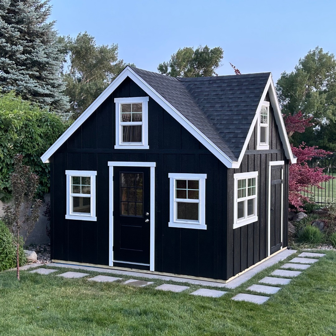 Black wooden shed with white trim and gable roof, featuring multiple windows and a front door, perfect for backyard or garden use.