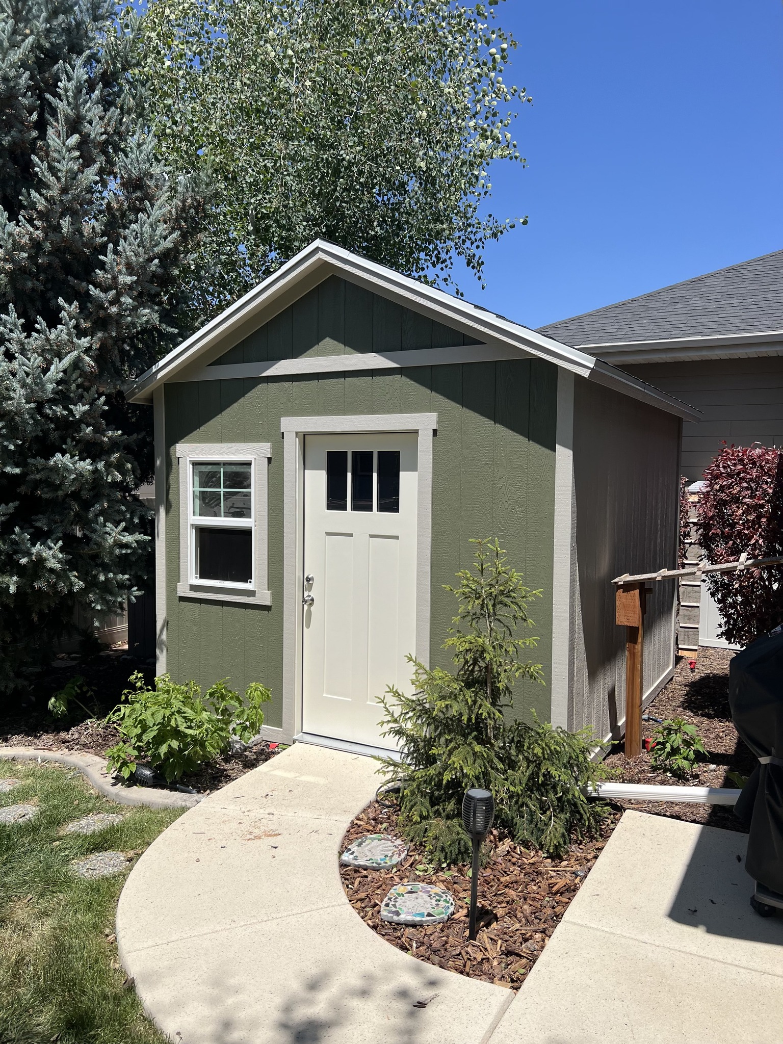 Green and white backyard shed surrounded by landscaping, representing Wright’s Shed Co.’s quality craftsmanship and durable sheds of Idaho.