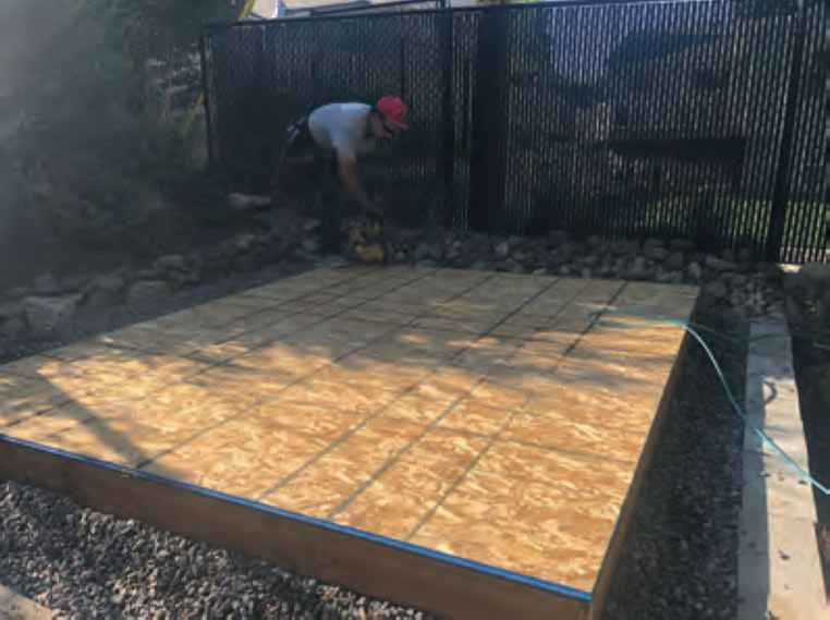 Worker securing tongue-and-groove OSB floor panels onto a pre-cut wood base during the installation of a Wright’s Shed Co. DIY shed kit.
