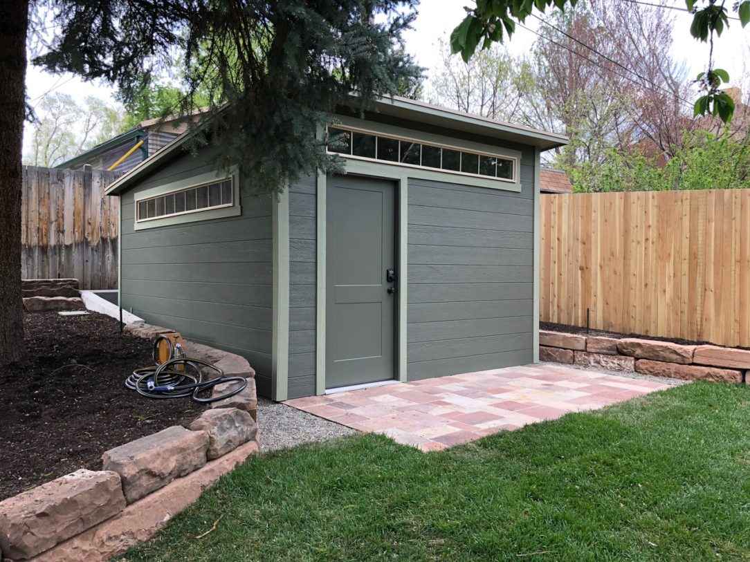 Modern Gray Lean-To Shed A sleek gray lean to shed with windows and a single door, surrounded by a wooden fence and garden, ideal for local rent to own sheds.