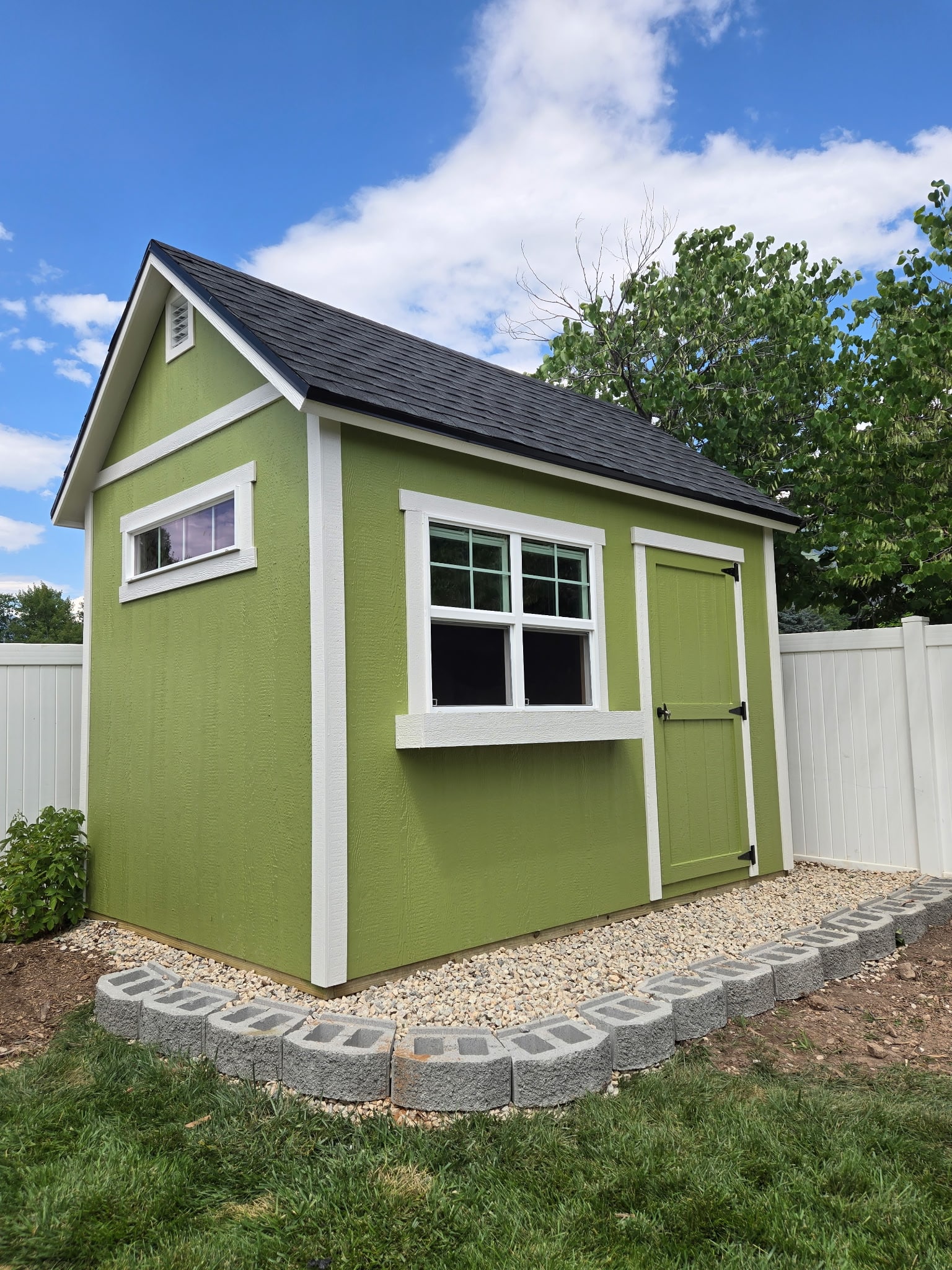 A green orchard-style shed with white trim and a front-facing window, perfect for use as outdoor workshop buildings in small spaces