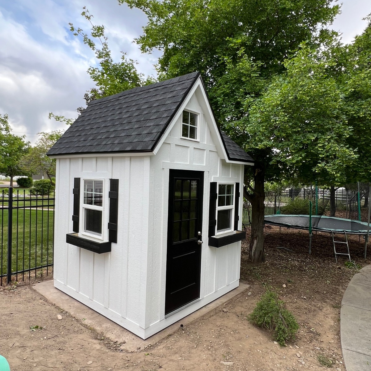 Compact white and black custom-built shed with windows and shingled roof, designed by Wright’s Shed Co. for backyard use and family enjoyment.
