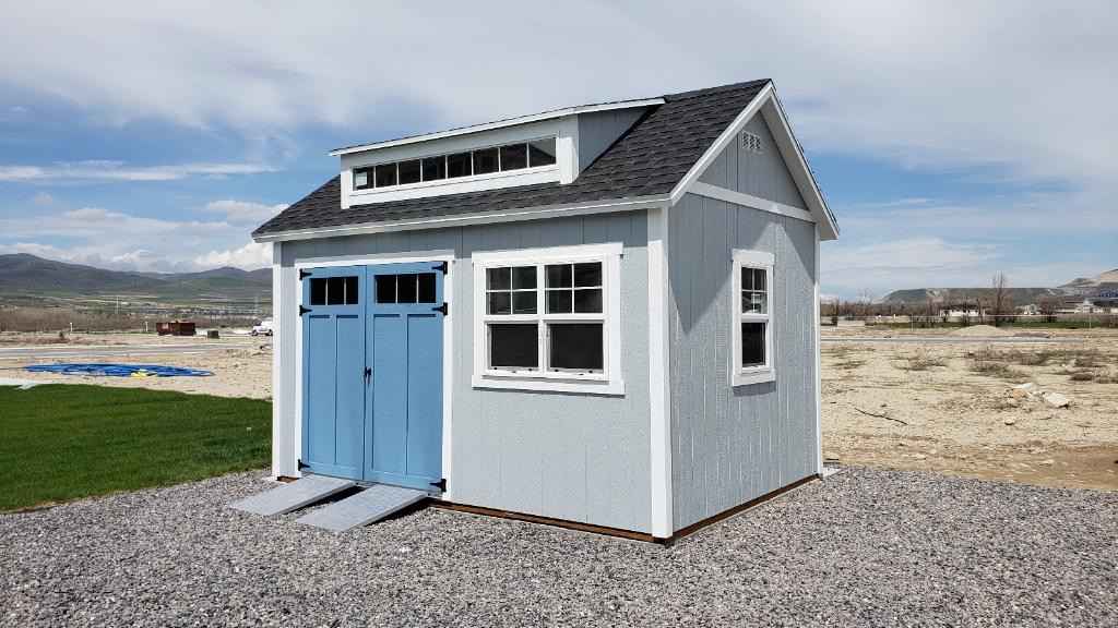 Gray backyard storage shed with blue double doors, showing how much do shed builders charge for quality shed designs.